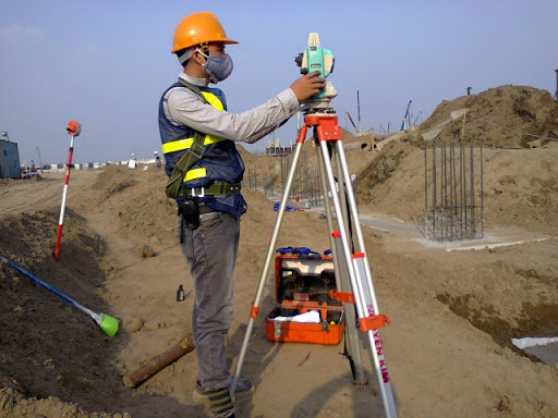 Kỹ sư trắc địa cầm bộ máy GNSS RTK Topcon HiPer HR đang cắm tiêu đo ranh đất tại một lô nền phân lô huyện Nhơn Trạch, Đồng Nai, bối cảnh xung quanh là nhà dân và đường đất đỏ